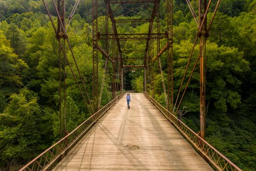 Aerial view of a senior woman walking her dog across the historic metal truss Jenkinsburg Bridge near Morgantown over Cheat River