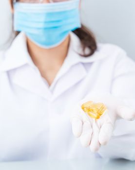 Close up Scientist hands putting in nitrile latex gloves holding Omega 3 capsule in labcoat wearing nitrile gloves, doing experiments in lab