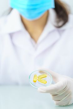 Close up Scientist hands putting in nitrile latex gloves holding Omega 3 capsule in labcoat wearing nitrile gloves, doing experiments in lab