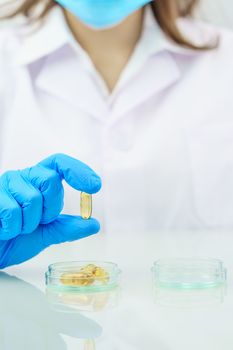 Close up Scientist hands putting in nitrile blue latex gloves holding Omega 3 capsule in labcoat wearing nitrile gloves, doing experiments in lab