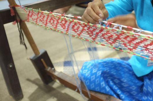 Woman Take Off Ties from Mudmee Board Weaving. Mudmee is a pattern of fabric. By using waterproof material to tie the cotton threads into the desired pattern Before dyeing cotton