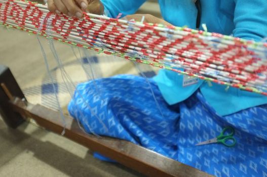 Woman Take Off Ties from Mudmee Board Weaving. Mudmee is a pattern of fabric. By using waterproof material to tie the cotton threads into the desired pattern Before dyeing cotton