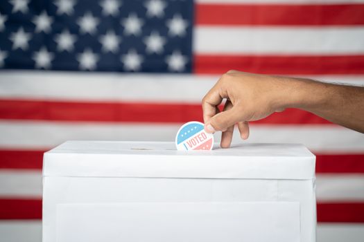 Concept of USA elections, Close up of Hands Putting I Voted sticker inside Ballot box with US flag as background