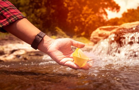 Close up of Woman's hand putting paper boat on the water and pushing it away with reflection sunshine in the water background, as in childhood.