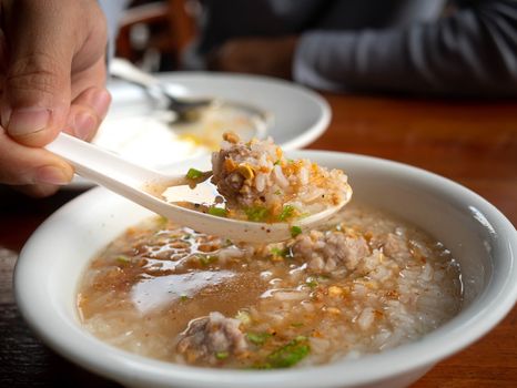 Close up of woman hand using spoon scooping the boiled rice with pork and fried garlic in a white bowl on breakfast.