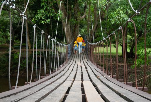 Rear view of family walking on suspension wooden bridge with nets or rope handrails in the park.