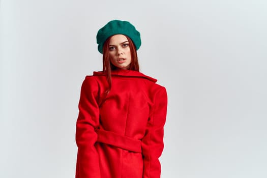 A woman holds in her hand a red coat and a dark T-shirt Green hat cropped view of a light background. High quality photo