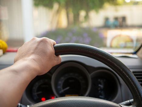 A man's hand held the steering wheel of a car to steer while the car was moving away. Concept and direction of business operations according to the plan.