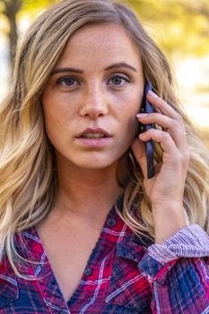 A gorgeous blonde model talks on her cellphone on an autumn day outdoors in a park