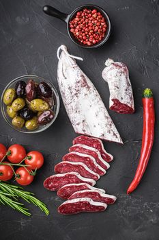 Spanish longaniza salami sausage slices with herbs on black textured background, topview.