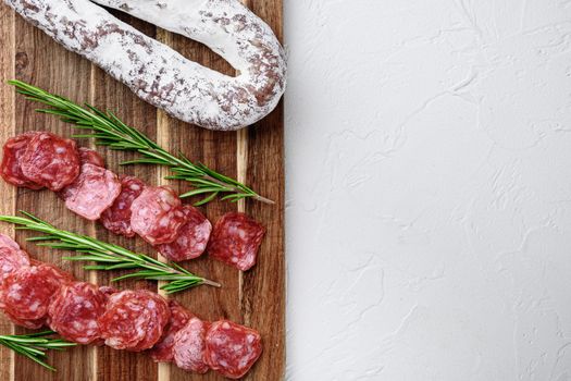 Fuet whole and sliced cuts, spanish dry cured sausage on white surface, top view with copy space.