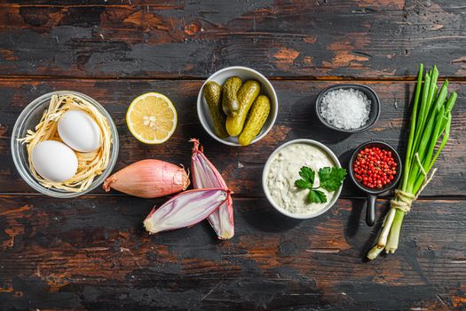 Organic tartar ingredients in a row pickles, capers, dill, parsley, garlic, lemon over old wood table and space for text on top and bottom.