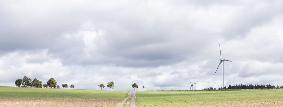 empty country road between fields on high plane neer Cochem in german eifel under cloudy sky in summer with wind turbines