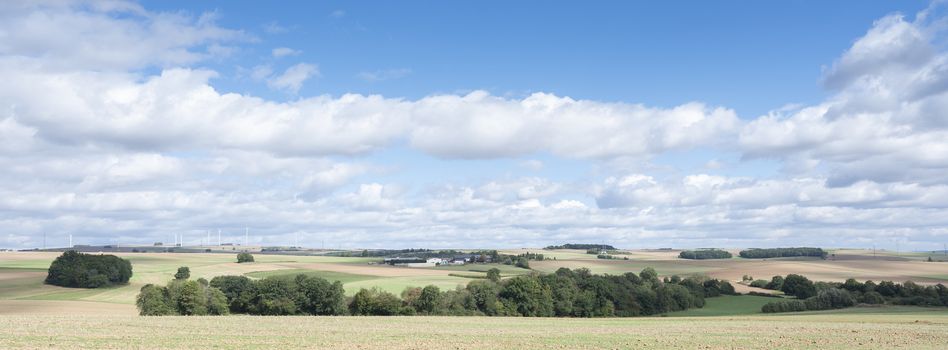 farm and fields on high plane neer Cochem in german eifel under cloudy sky in summer with wind turbines
