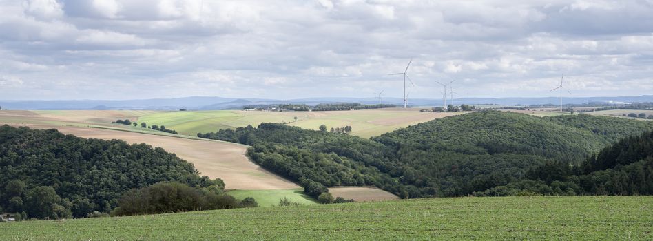 fields and wiind turbines in german eifel under cloudy sky in summer