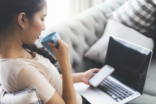 Woman working on laptop and drinking coffee while sitting in a big comfortable chair at home.