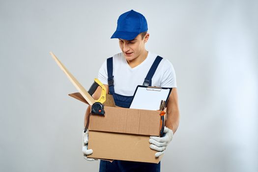 man in working uniform with a box in his hands tools loader delivery light background. High quality photo