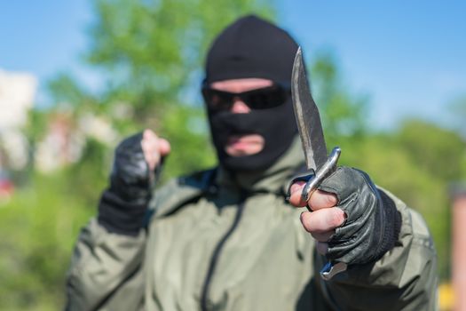 A hunting knife in the hands of a man in a balaclava