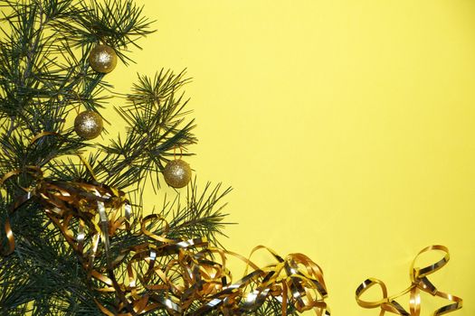 coniferous branches and Christmas tree decorations on a New Year's yellow background, copy space.