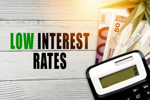 LOW INTEREST RATES text with currency banknotes, decorative plant, and calculator on wooden background. Business concept