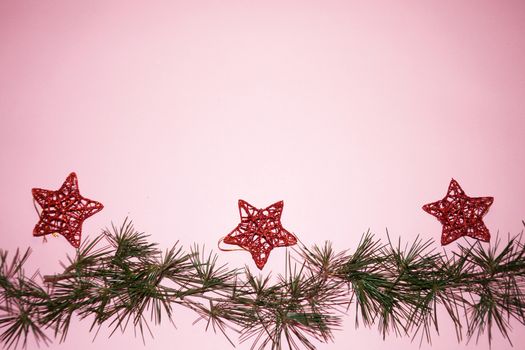 coniferous branches and Christmas tree decorations - red stars on a New Year's pink background, copy space.