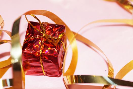 shiny red gift box and gold ribbon on pink background close up