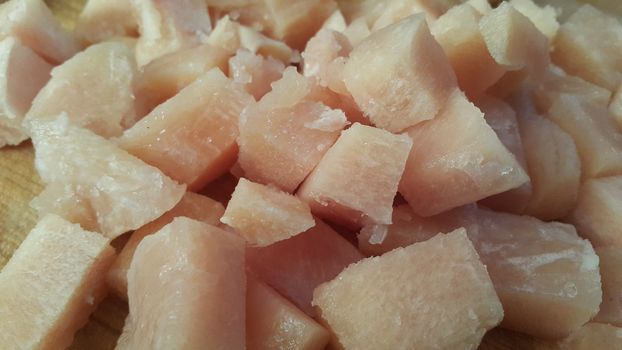 Close up top view of fresh finely chopped chicken meat cubes. White meat small steaks with meat fat.