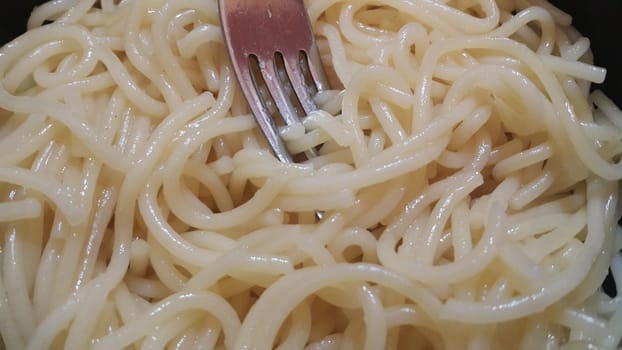 close up view of swirling noodles or spaghetti pasta in a bowl with silver fork