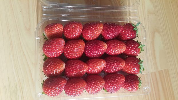 Healthy, fresh organic strawberries in supermarket for sale, pile of strawberries placed in transparent tray over wooden floor