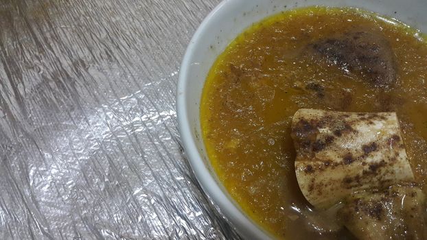 Top view of siri paaye or paya dish garnished with diced ginger, long coriander leaves and fresh sliced lemon. This dish is popular in Pakistan and Bangladesh
