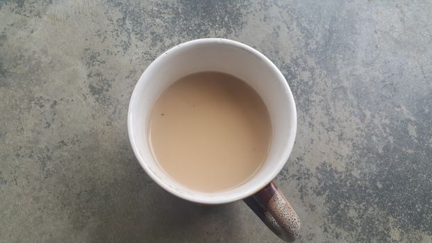 Beautiful coffee white mug with black milk-tea over concrete grey floor. A top view of tea cup filled with tea.