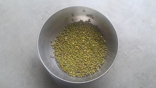 Closeup view of green whole Mung bean or green gram, maash, or moong in a bowl on floor. It is used as an ingredient in both savory and sweet dishes.