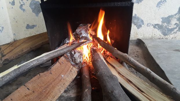 Fire on logs in fire pot with embers and burning coal. Bonfire with blazing red and orange fire flames. Fire background with woods and planks on fire at night view.