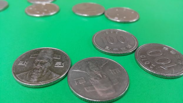 Silver shining Korean won coin scattered over a green floor.