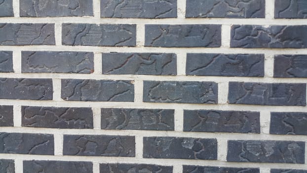 Closeup texture of black brick wall. A background of a weathered old exterior brick wall in the sunshine.