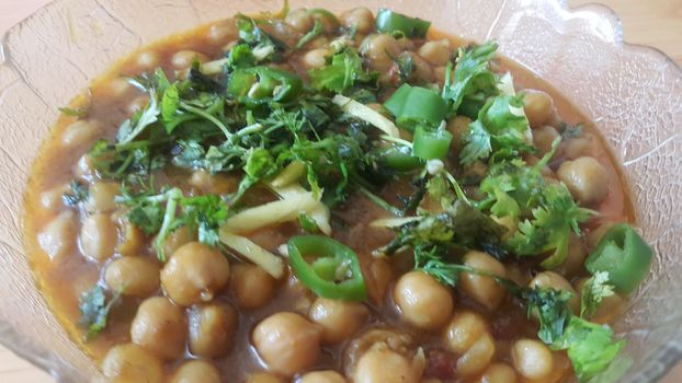 Home made dish served in glass bowl garnished with sliced onion and green coriander leaf and placed over wooden floor .Traditional lentils Channa Masala or chickpeas curry or chole bhature.