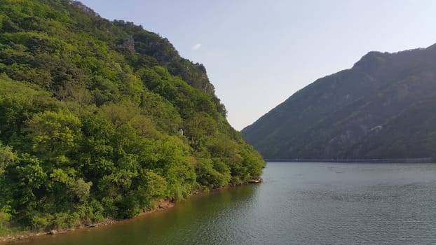 View of beautiful scene of river water and green trees on large hills on a sunny day with blue sky in background. A lovely landscape with breathtaking view over the horizon .