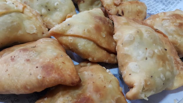 Closeup of delicious home made spicy and crunchy samosa pastries placed in a white ceramic plate on wooden floor