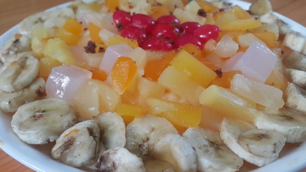 Creamy tasty sweet fruit trifle over custard with banana slices layered on surface on wooden floor. A top view of home made fruit trifle, a products for dessert after meal.