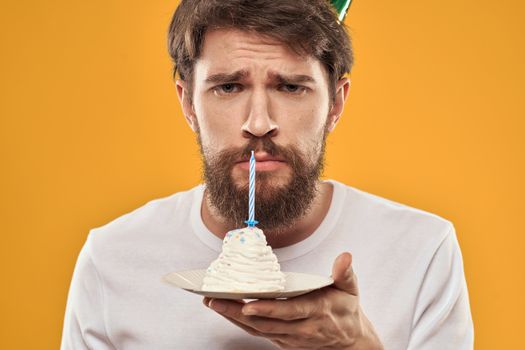 Handsome man with a beard and in a cap celebrating a birthday party yellow background. High quality photo