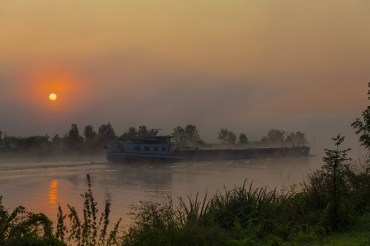 boat in the maas during sunrise in the early morning  in limburg in holland with the trees mist and hazy fog