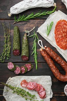 Variety of dry cured chorizo, fuet and other sausages cut in slices with herbs on dark wooden background, topview.