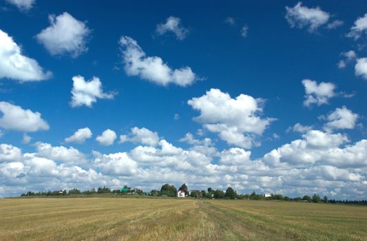 Countryside summer landscape with many white clouds flying over field and with a village on skyline