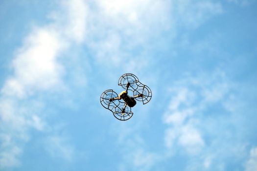 Drone contour with engine protection grid flying in the blue sky with calm white clouds view bottom to top