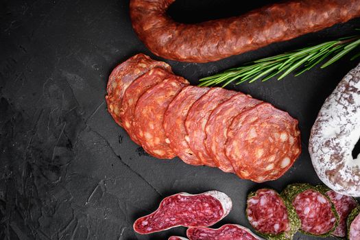 Set of dry cured salami, spanish sausages, slices and cuts on black textured surface, topview.