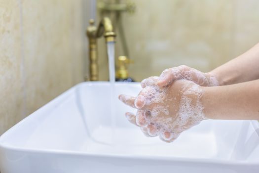 Woman washing and disinfecting hands with soap and hot water as part of coronavirus prevention and protection protocols; stop spreading covid-19 hygiene protocols. Focus on her finger.