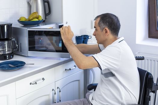 Young Man in Whellchair Using Microwave Oven For Baking In Kitchen. Focus on his hand.