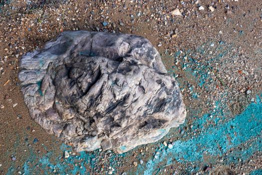 The stone lies in the sand on the coast.Nearby is a turquoise strip of river foam from the fuel.The concept of the environment.