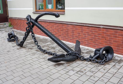 An old black anchor lies on the sidewalk.