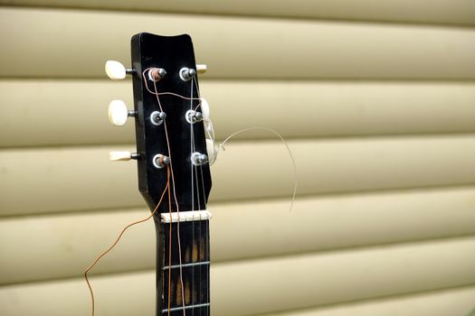 Guitar neck and head in bad condition with broken strings in front of house wall side view close up